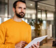 Mann verwendet Tablet in der Hand, steht in einem modernen Büro.