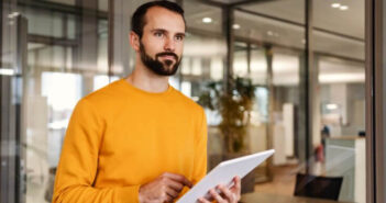 Mann verwendet Tablet in der Hand, steht in einem modernen Büro.