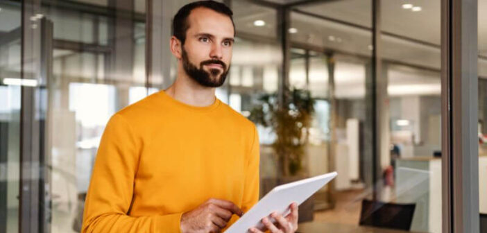 Mann verwendet Tablet in der Hand, steht in einem modernen Büro.